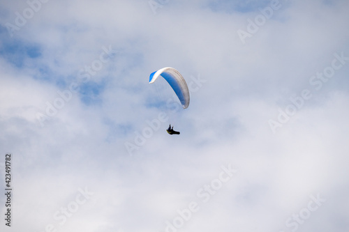 Paraglider flying like a bird in blue cloudy sky.