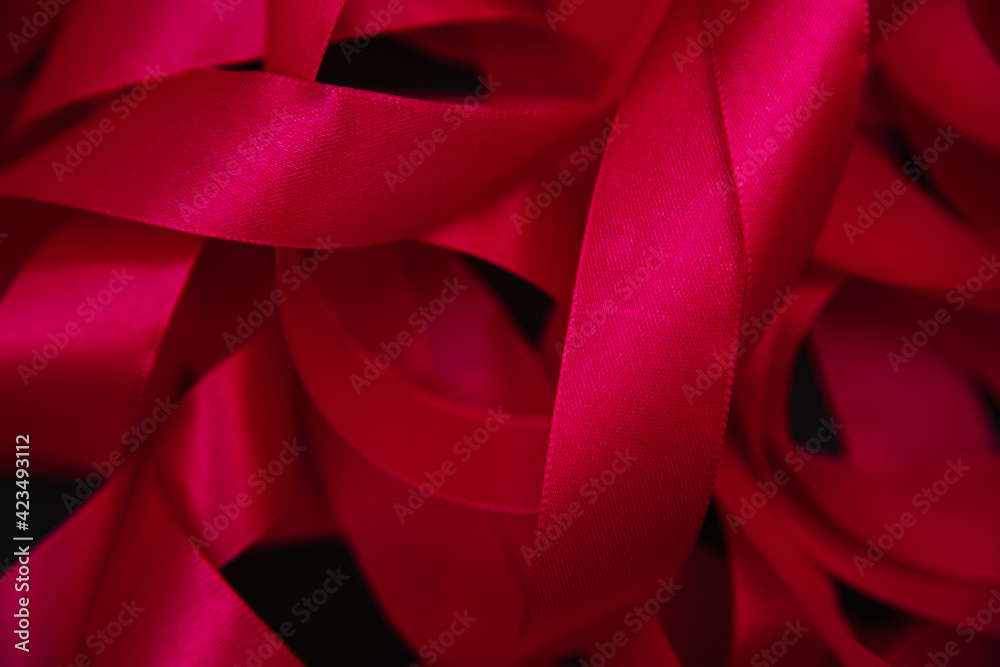 A red satin ribbon lies on a black background. Minimalistic photography.Festive background and texture.