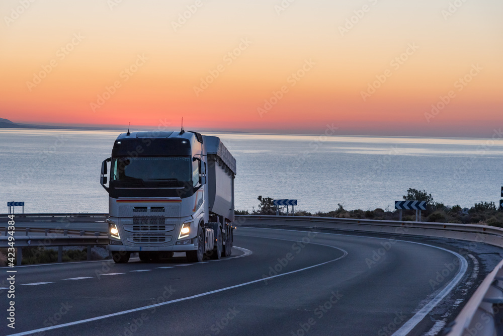 Dump truck on a mountain road by the sea with a sunrise background.