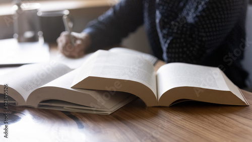 Close up woman student writing notes from textbook, sitting at desk with books, young female preparing for university or college exams, doing homework, school assignments at home, education concept photo