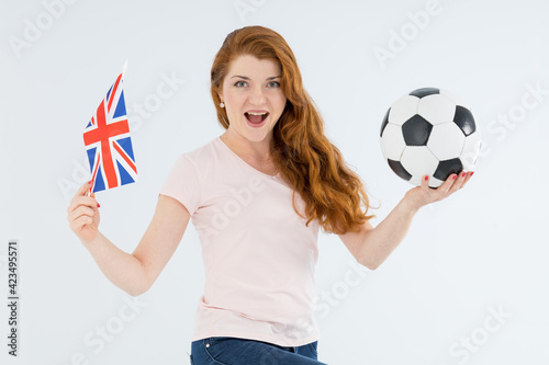 Happy red hair woman, soccer fan with ball and Great Britain flag, isolated on gray background. photo