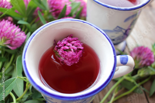 Cup of tea with pink flowers. Herbal tea or infusion with red clover on the wooden table. Natural floral background. Top view
