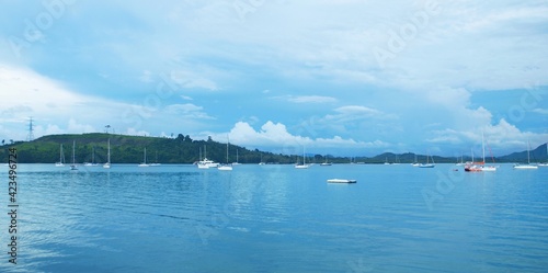 Panoramic view of sea bay. Land with green hills on the horizon. Blue sky with clouds. Calm water. Sailing yachts in the harbor. Wide frame, seascape, tropical resort. Thailand, Phuket island, boats