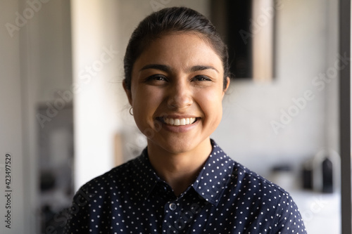 Head shot portrait smiling Indian young woman looking at camera, standing at home, attractive female blogger shooting vlog for social network, teacher coach recording webinar, profile picture