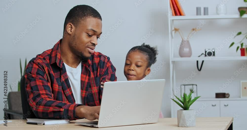 Afro american man sits at table at computer looks at screen typing little loving daughter girl hugs dad stops work closes laptop requires attention gently cuddles to parent, concept of love and care