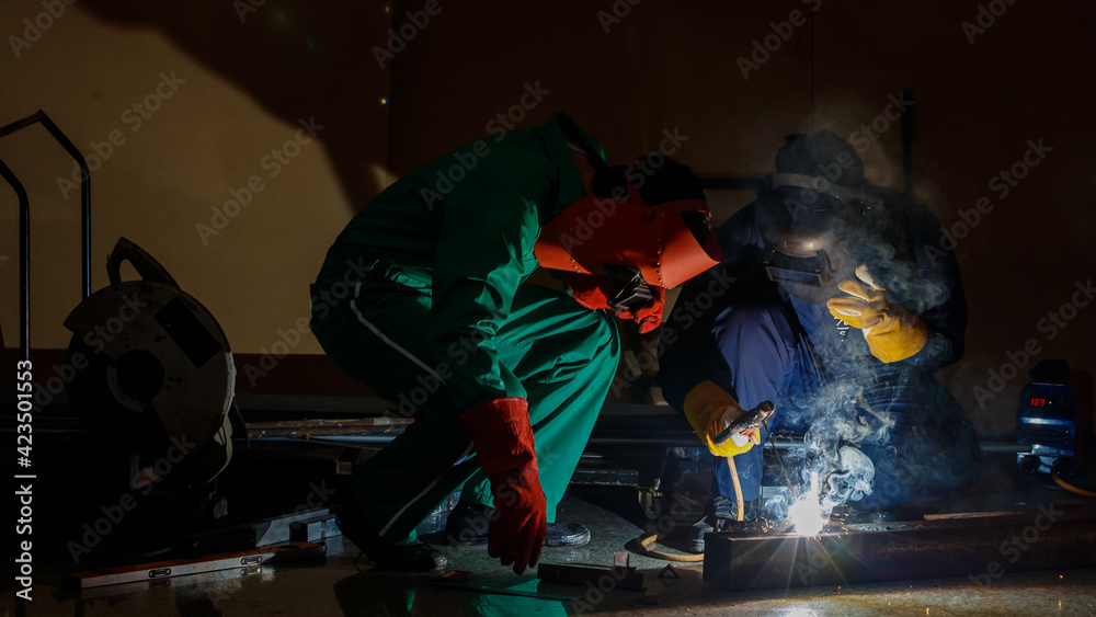 mechanics workers work overtime hardly at night in a factory. Engineers wearing safety outfits with mechanic jumpsuits, gloves, boots, and welding helmets working on metal welding mechanics workers work overtime hardly at night in a factory. Engineers wearing safety outfits with mechanic jumpsuits, gloves, boots, and welding helmets working on metal welding