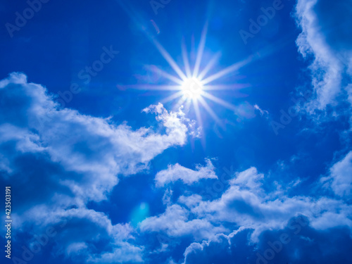 Clear sky with bright sun and rays in the atmosphere  below are light fluffy clouds