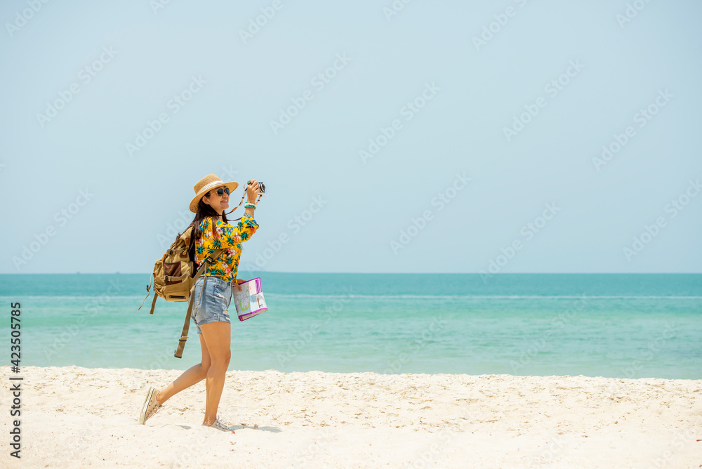 Asian woman traveler with backpack holding  map take photo on the beach enjoy life