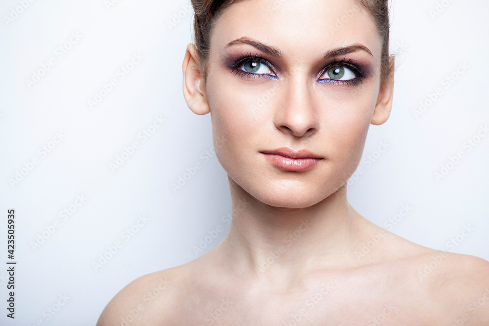 Front closeup portrait of a beautiful female model with bare shoulders with makeup, over light background. Front closeup portrait of a beautiful female model with bare shoulders with makeup, over light background.
