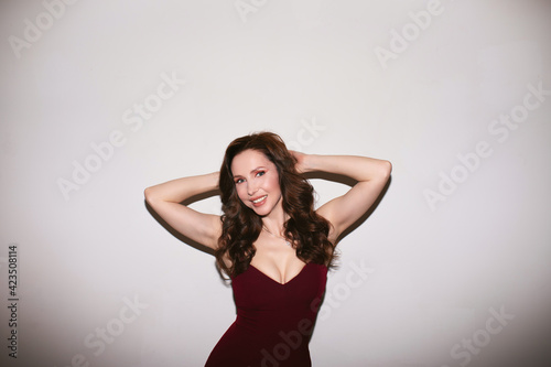 Attractive slim woman in wine dress with make up and curly long hair posing on white background. Copy space.