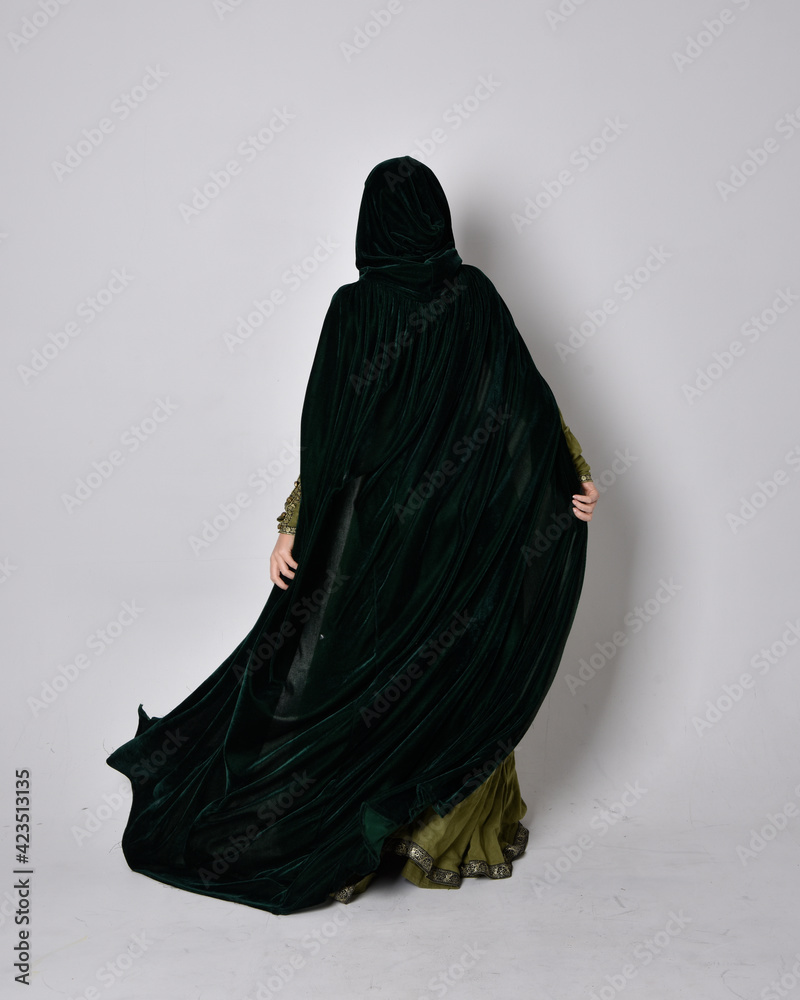 full length portrait of red haired girl wearing celtic, green medieval gown with fantasy velvet cloak. Standing pose isolated against a studio background. full length portrait of red haired girl wearing celtic, green medieval gown with fantasy velvet cloak. Standing pose isolated against a studio background.