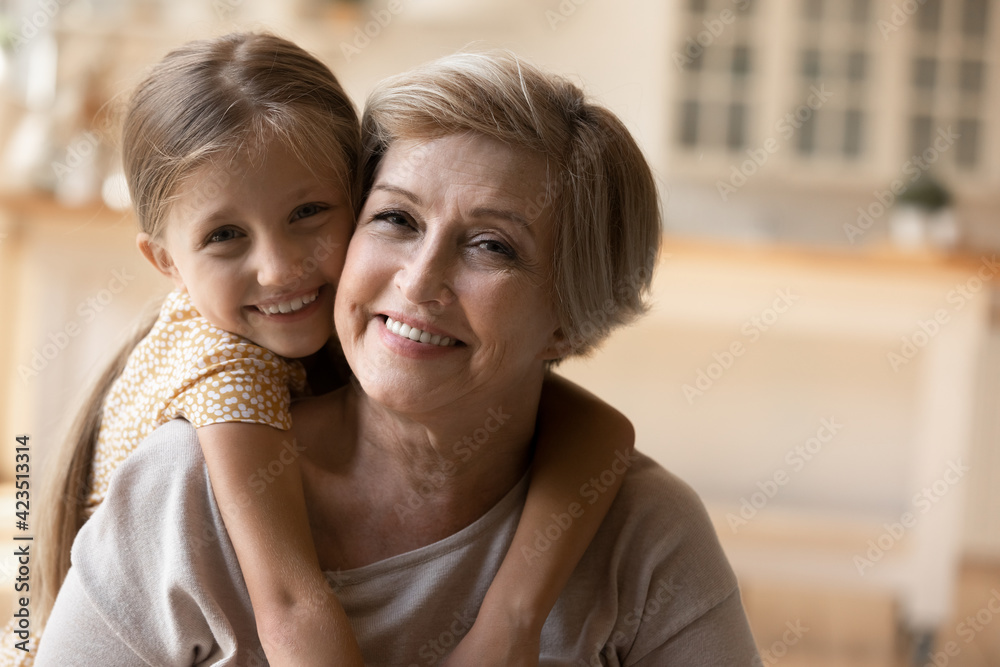 Close up portrait of cute little 9s girl child hug cuddle smiling mature 60s grandmother feel grateful and thankful. Happy small granddaughter and senior granny embrace show love and care in family. Close up portrait of cute little 9s girl child hug cuddle smiling mature 60s grandmother feel grateful and thankful. Happy small granddaughter and senior granny embrace show love and care in family.
