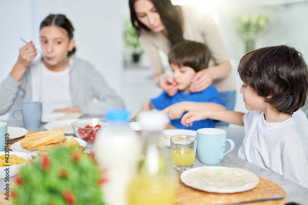 Cute little hispanic boy having breakfast together with his mom and siblings. Latin family enjoying meal together, sitting at the kitchen table at home