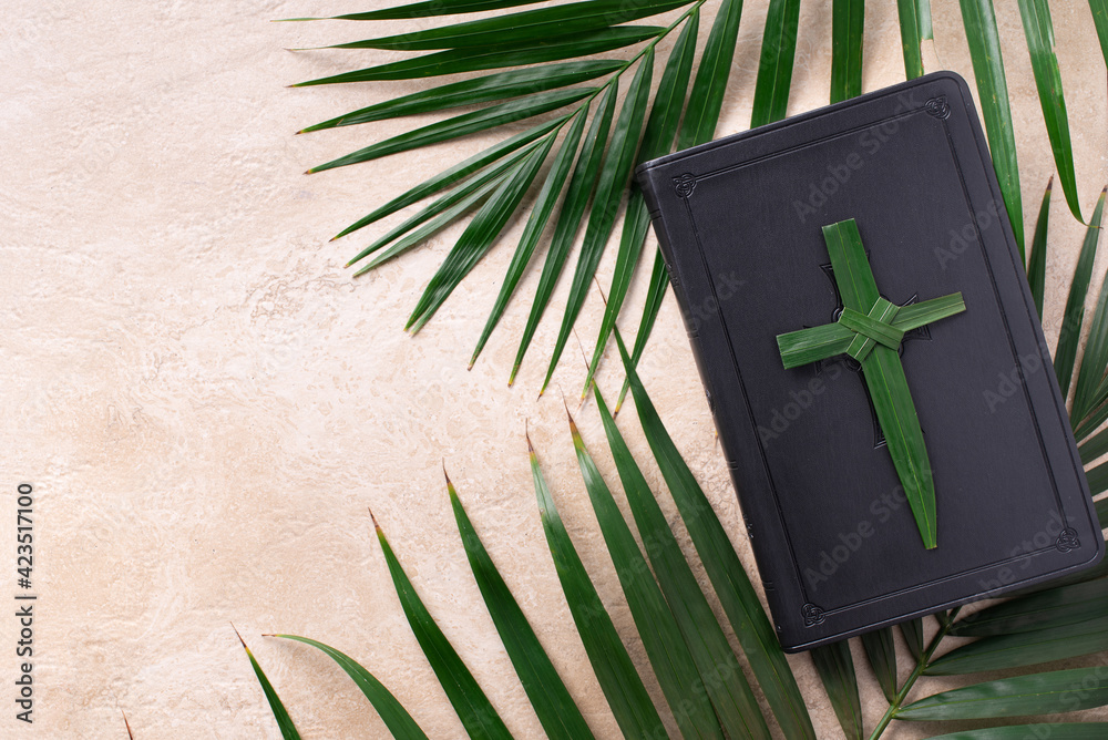Palm Sunday concept. Palm cross on open Holy Bible and palm leaves