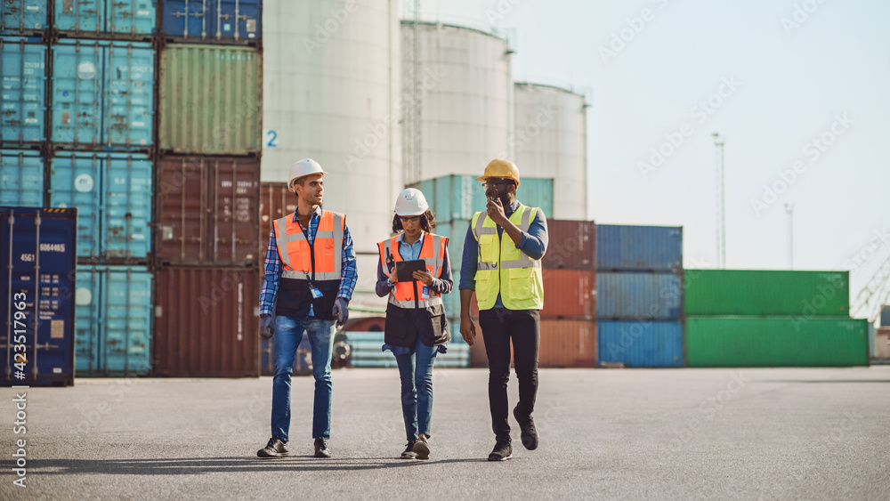 Team of Diverse Industrial Engineers, Safety Supervisors and Foremen in Hard Hats and Safety Vests Walking in Shipping Cargo Container Terminal Depot. Colleagues Talk About Logistics Operations.