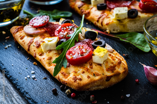Focaccia - roasted mozzarella sandwiches with salami pepperoni, feta cheese and tomatoes on black stone plate
