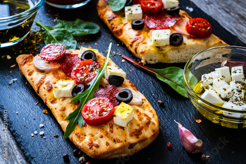 Focaccia - roasted mozzarella sandwiches with salami pepperoni, feta cheese and tomatoes on black stone plate
