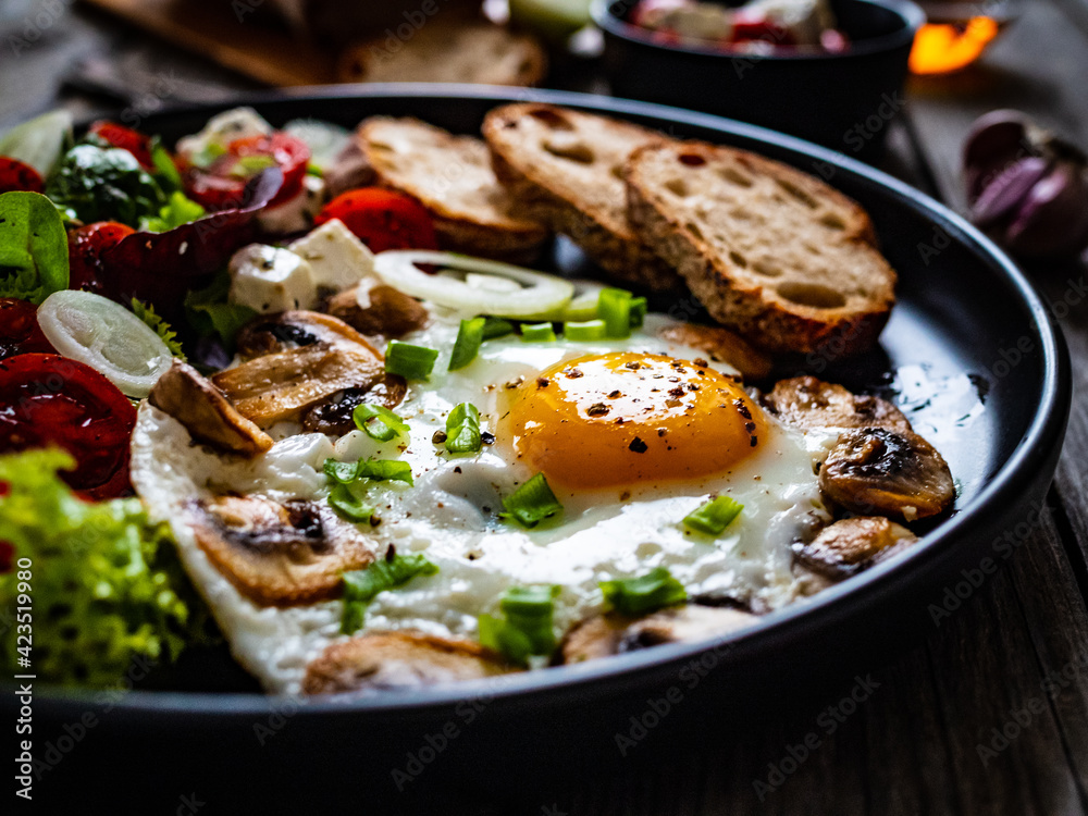 Continental breakfast - sunny side up eggs on white mushrooms, onion and greek salad on wooden table
Continental breakfast - sunny side up eggs on white mushrooms, onion and greek salad on wooden table
