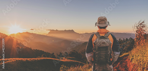 Hipster male hiker with backpack enjoying sunset on peak mountain. Tourist traveler on background view mockup.