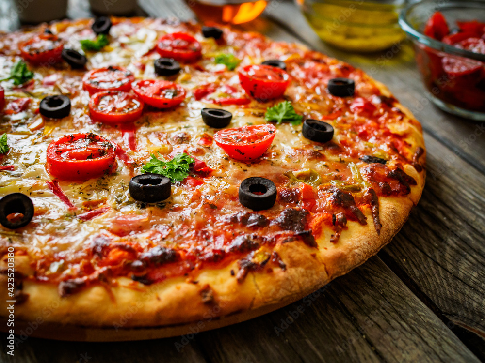 Pizza with ham, tomatoes, olives, parmesan and mozzarella on wooden background
