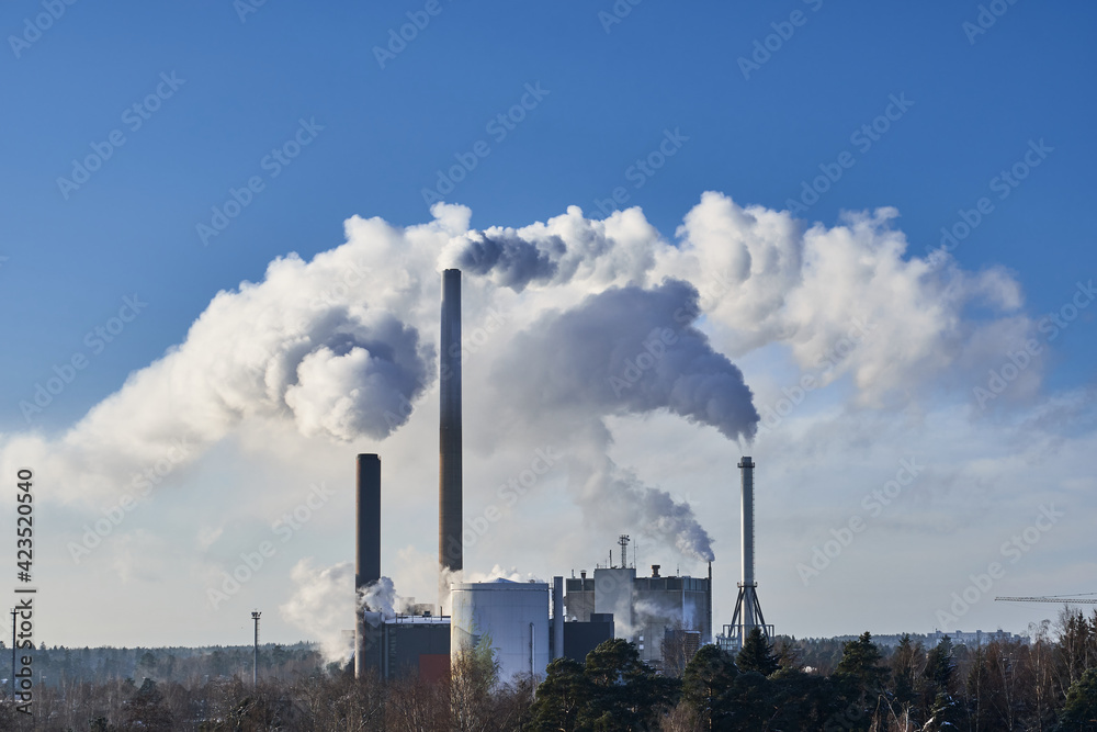 Close-up view of CHP plant pipes with smoke in the sunny day.