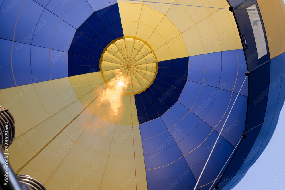 Fototapeta premium Die Flamme, die die Luft im Inneren eines gelb und blauen Heißluftballons erhitzt