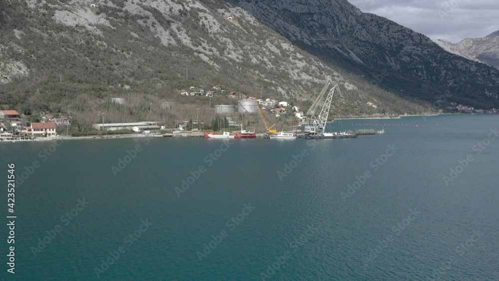 Drone flies over the sea towards the coast, to the industrial pier, where there is a ship's crane and industrial transport - boats and ships Drone flies over the sea towards the coast, to the industrial pier, where there is a ship's crane and industrial transport - boats and ships