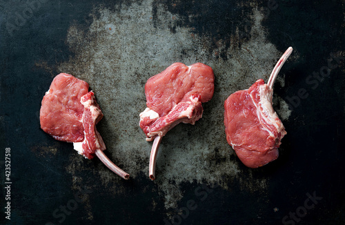 Raw veal Frenched Racks meat with ingredients on rustic dark background
