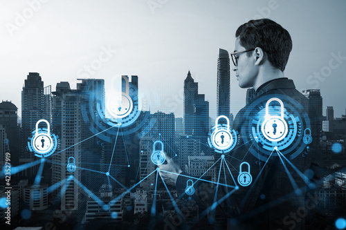 A young handsome eastern cybersecurity developer explores new approaches to protect clients confidential information using phone. IT lock icons over Bangkok city background.