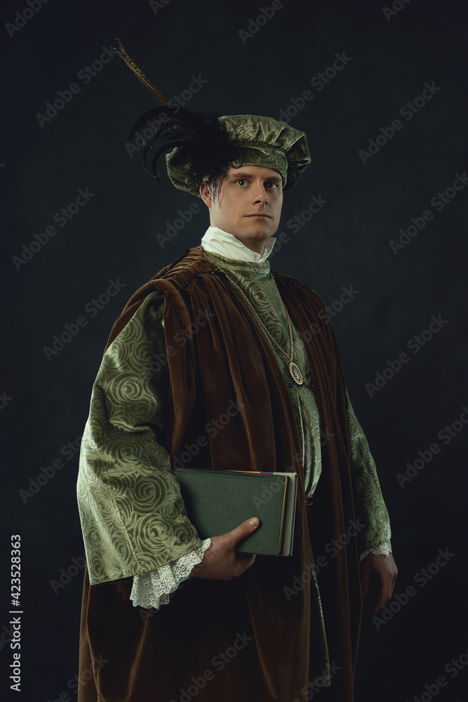 Renaissance man holding a book stands in front of a dark wall.