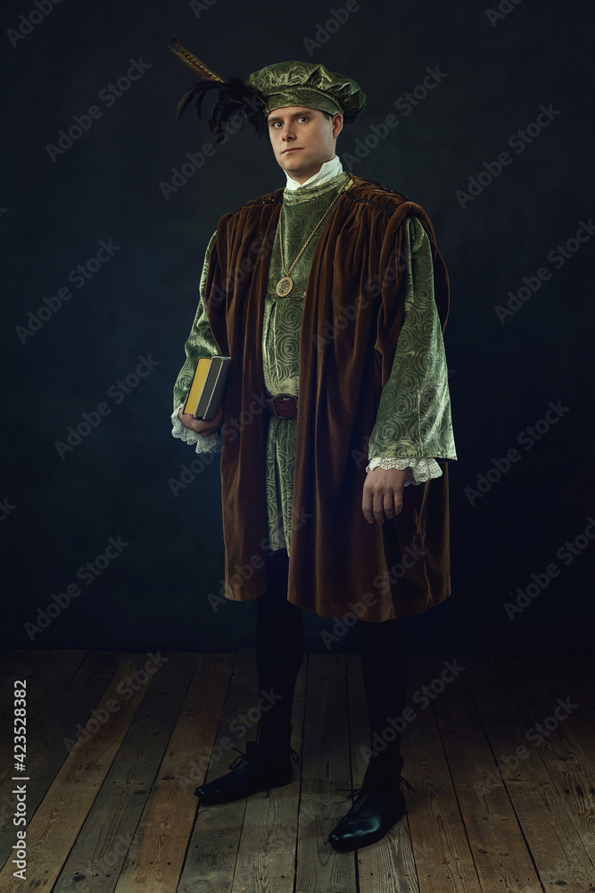 Renaissance man holding a book stands in front of a dark wall.