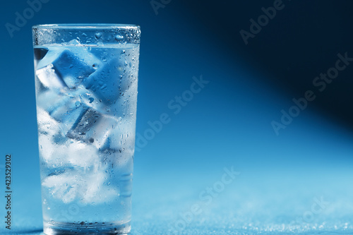 A glass with ice water and ice cubes on a blue background.
