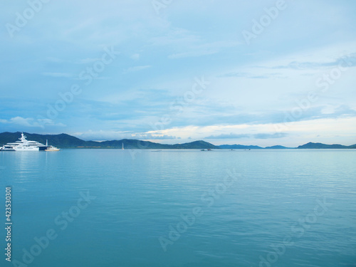 White big luxury yacht in the blue sea. Boat in left side of frame. Cloudy sky. Land on the horizon. Green hills on a coast. Coastline  calm water surface. Sea bay  seascape. Two yachts big and small