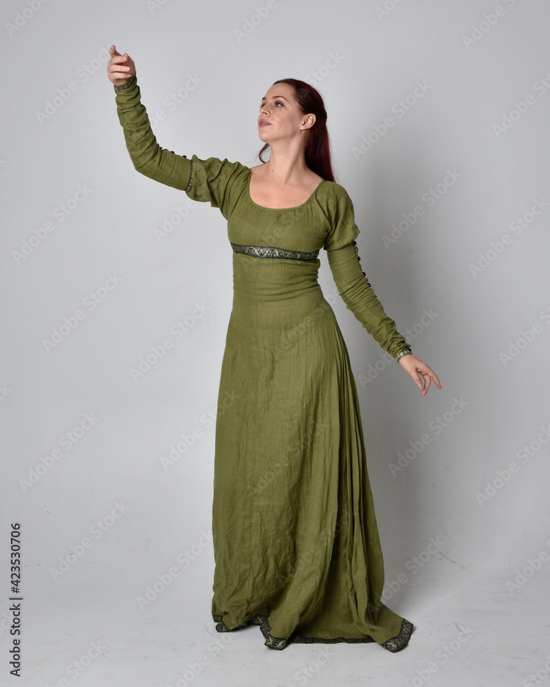 full length portrait of red haired girl wearing celtic, green medieval gown. Standing pose isolated against a studio background. full length portrait of red haired girl wearing celtic, green medieval gown. Standing pose isolated against a studio background.