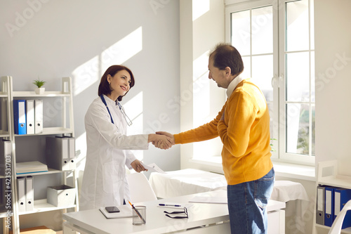 Healthy middle aged male patient shaking hand smiling young female doctor nurse thanking for good medical checkup result and successful treatment. Old people medical health care and trust concept