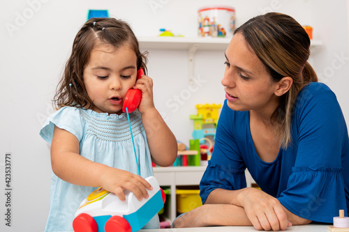 Little girl and her kindergarten teacher play with a toy phone, pretending to have conversations.