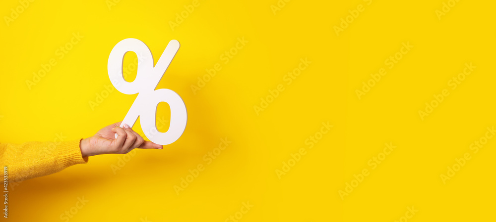 hand holding percentage sign over yellow background, panoramic image - obrazy, fototapety, plakaty 