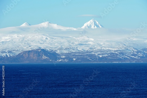 Mountains covered with snow in Aleutian Islands as a part of island chain in Alaska observed form container vessel sailing over Pacific ocean during sunny winter weather and calm sea. photo