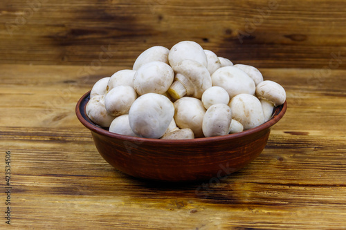 Fresh champignon mushrooms in ceramic bowl on the wooden table