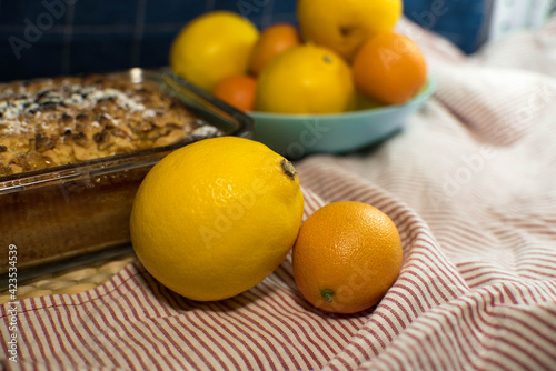 a delicious lemon shortbread pie in a glass baking dish and on a wooden board lies on a towel with ripe yellow and orange citrus fruits on a blue background
