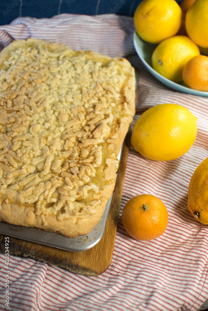 a delicious lemon shortbread pie on a metal baking sheet and wooden board sits on a striped towel with ripe yellow and orange citrus fruits a delicious lemon shortbread pie on a metal baking sheet and wooden board sits on a striped towel with ripe yellow and orange citrus fruits