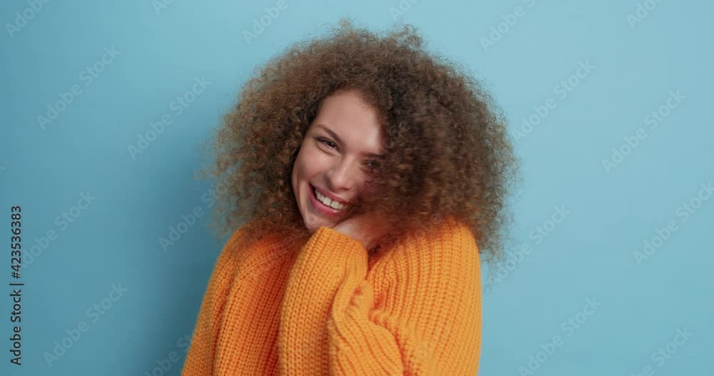 Pleased attractive curly haired young woman feels shy and happy while gets compliment from handsome man smiles toothily wears casual orange jumper isolated over blue background. Emotions concept Pleased attractive curly haired young woman feels shy and happy while gets compliment from handsome man smiles toothily wears casual orange jumper isolated over blue background. Emotions concept