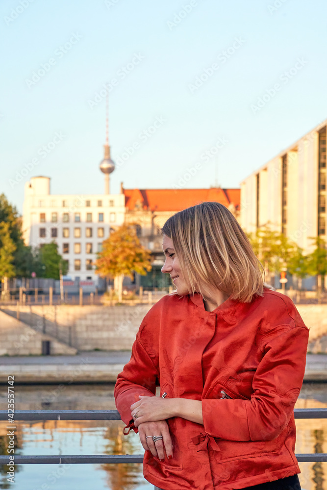 Portrait of smiling fashionable young woman in front of the Television Tower (Berliner Fernsehturm) in Berlin, Germany.
