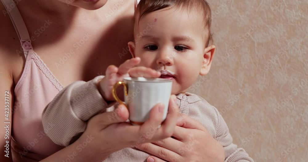 Portrait of a little boy who sits in his mother's arms. Happy child drinks milk or dairy product from a cup. Proper and natural nutrition for children Portrait of a little boy who sits in his mother's arms. Happy child drinks milk or dairy product from a cup. Proper and natural nutrition for children