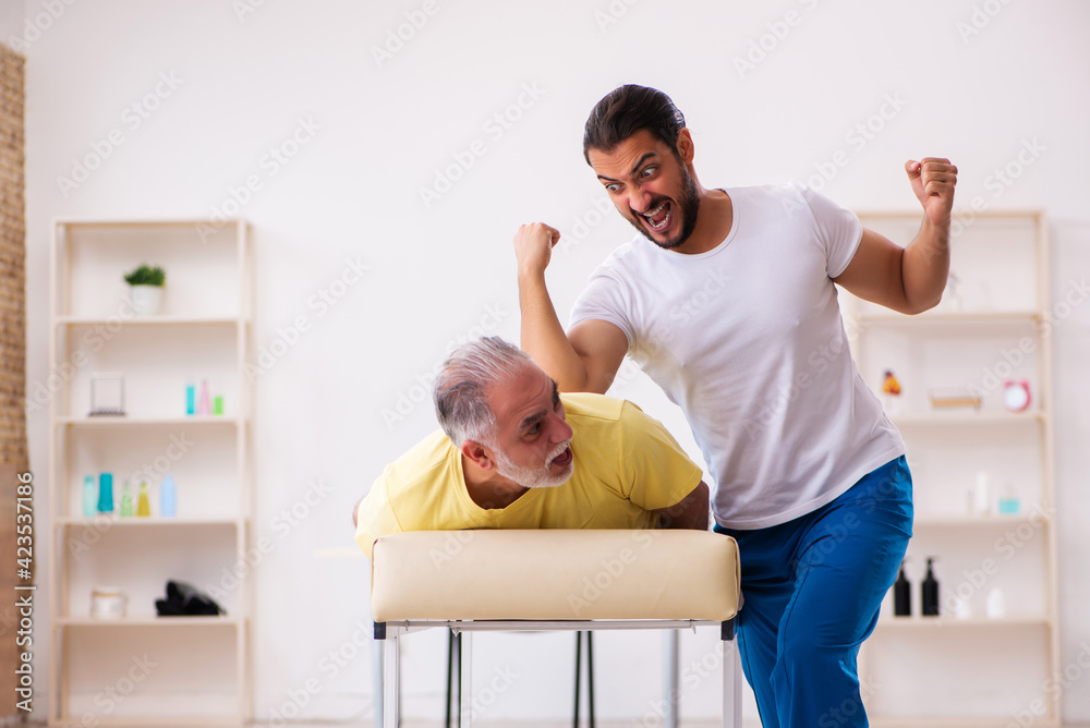 Obraz premium Old male patient visiting young male doctor chiropractor