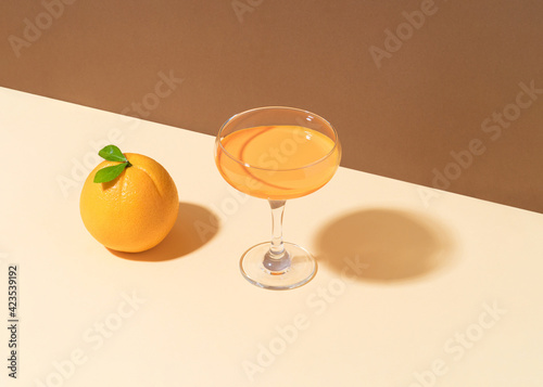 Minimal vintage  composition with orange fruit and cocktail glass on peach puff table. Duo tone background, sunny day.
