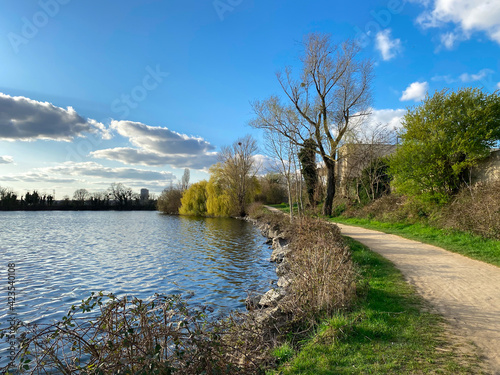 Pathway in front of a lake. Rural scene above the water at spring. Beautiful landscape with clouds in blue sky.