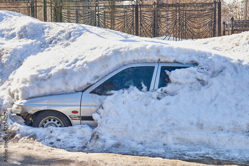 The old broken car is completely covered with snow.