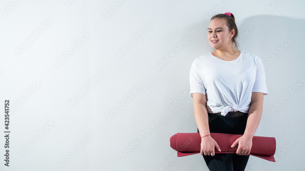 Obraz premium Young fat caucasian woman holding a sport mat. Charming plus size model in sportswear stands on a white background