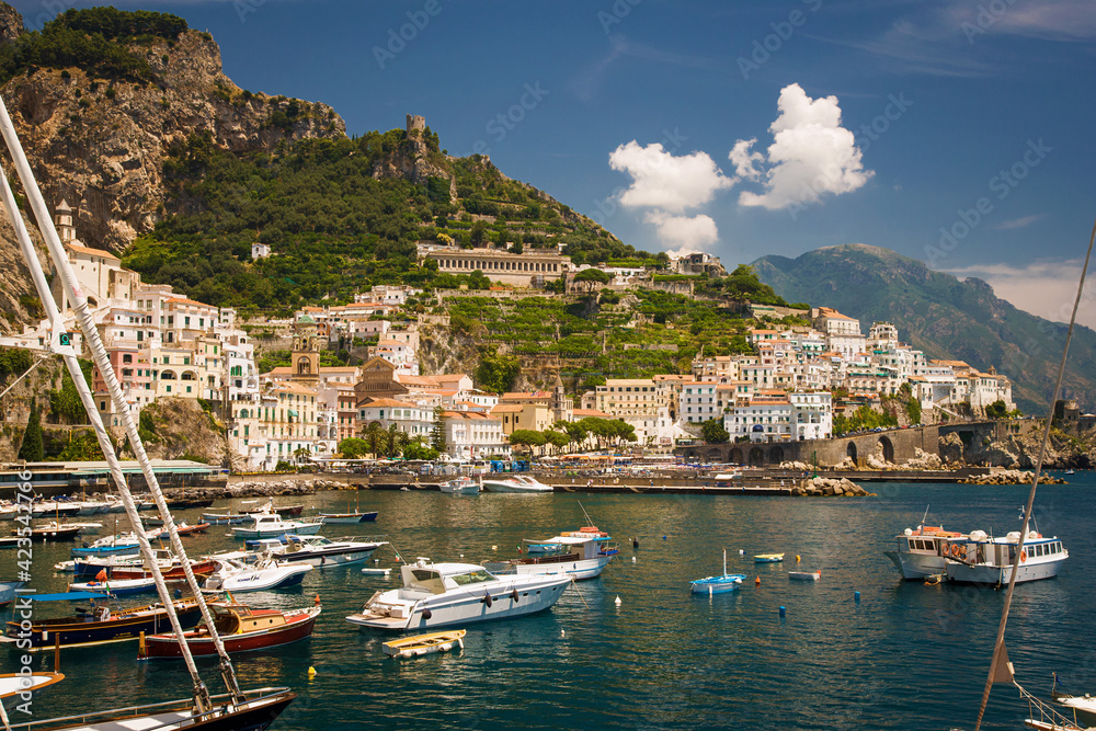 Amalfi Italy harbor with boats in foreground and town in background with blue sky and clouds